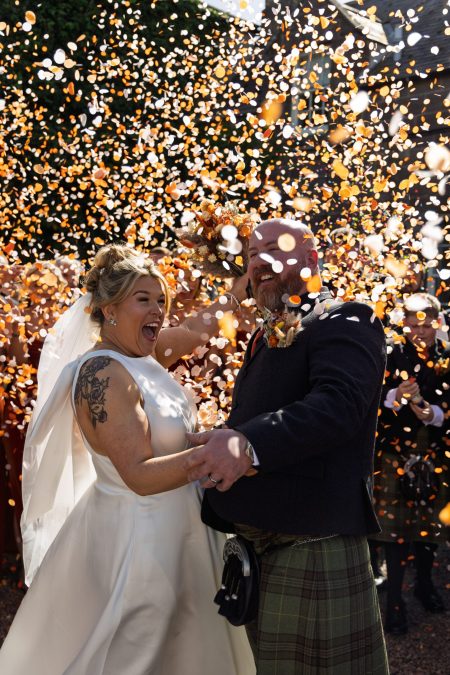 a shower of orange and white confetti covers a wedding couple who are cheering