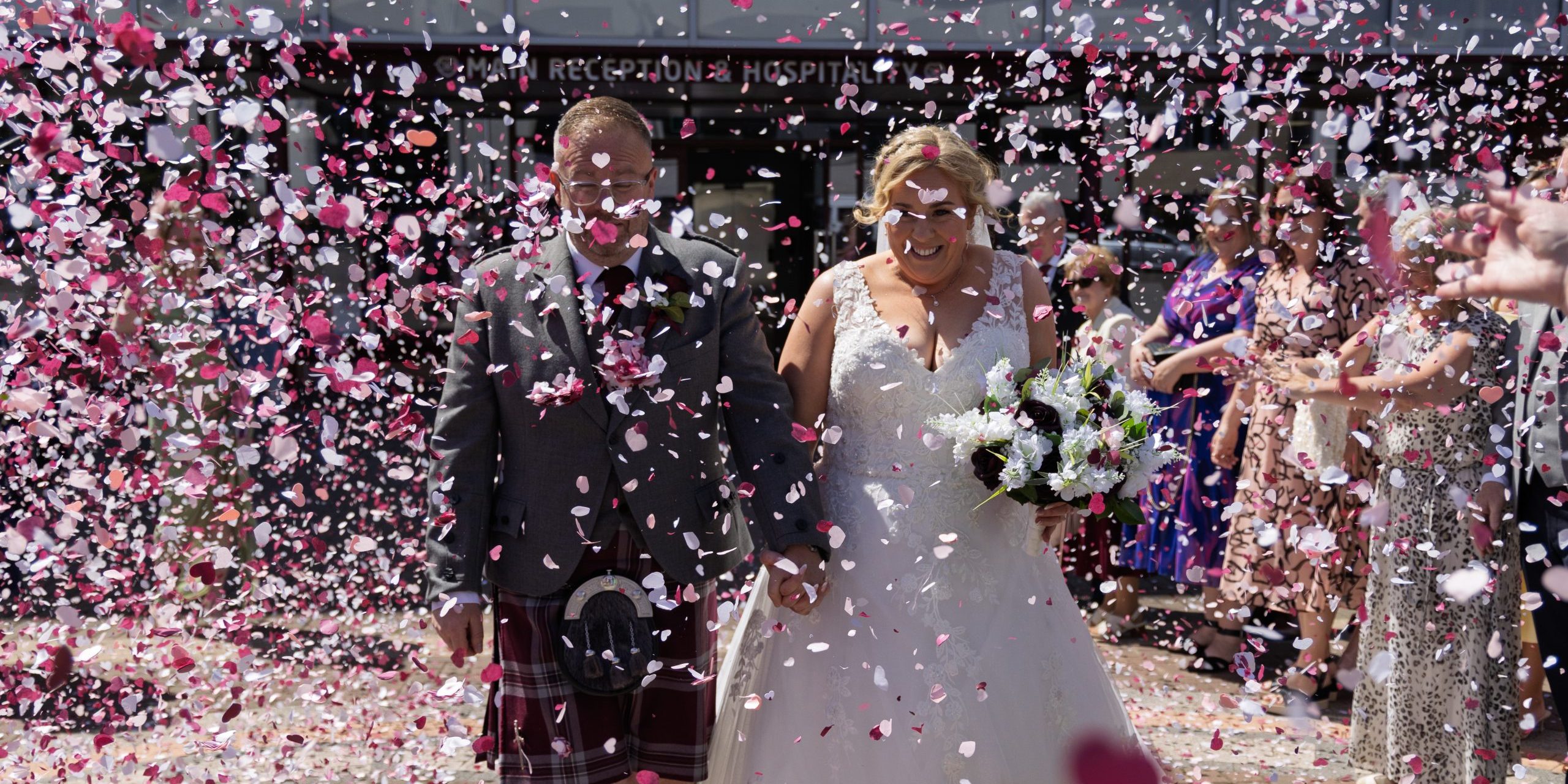 a hetero couple walking through a storm of maroon, white and pink confetti outside Tynecastle football stadium